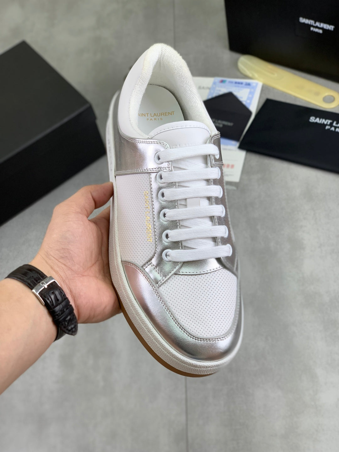 White and silver low-top sneakers with white laces, metallic trim, and gum sole.