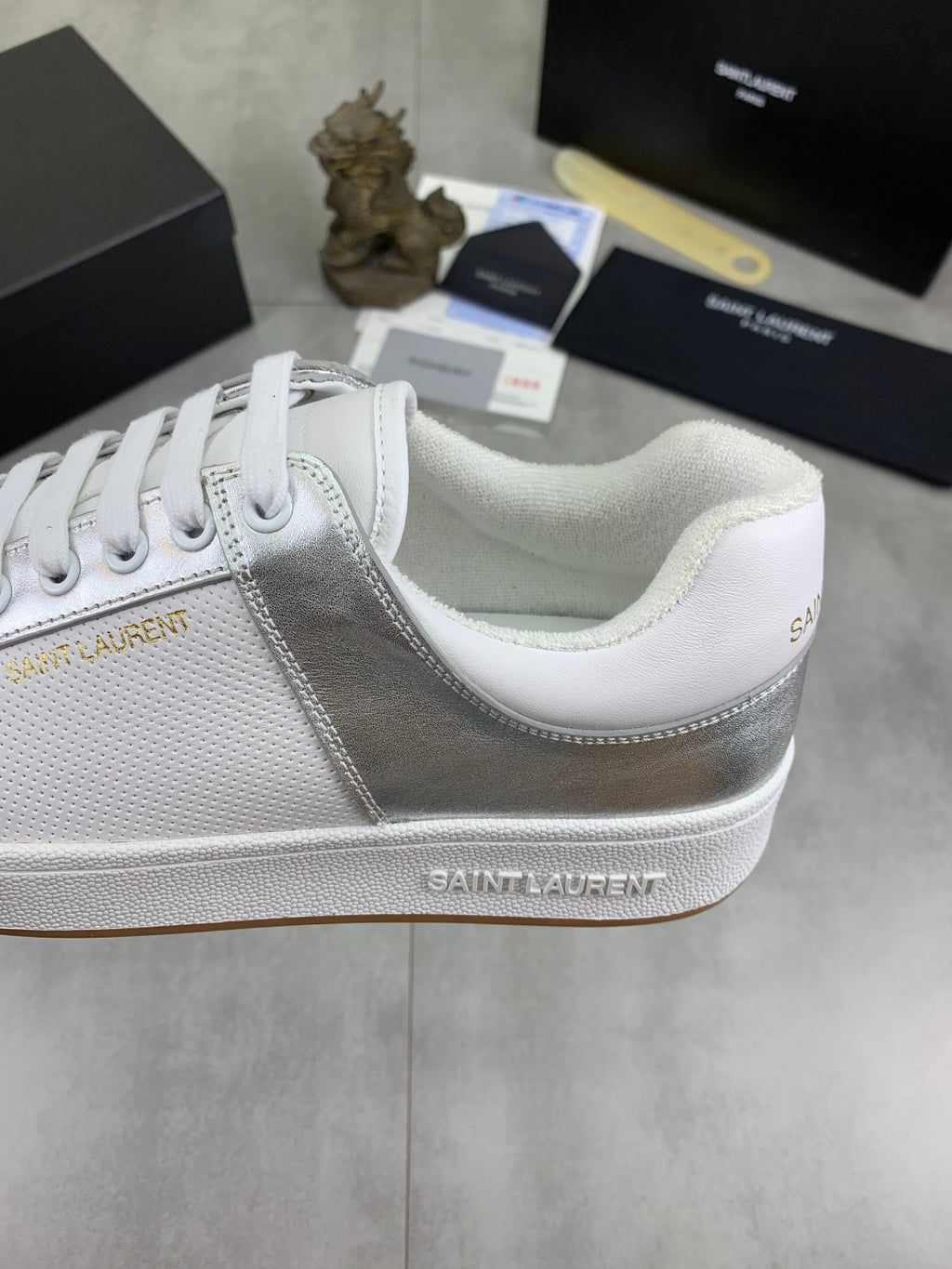 White and silver low-top sneakers with white laces and stitched panel detail.
