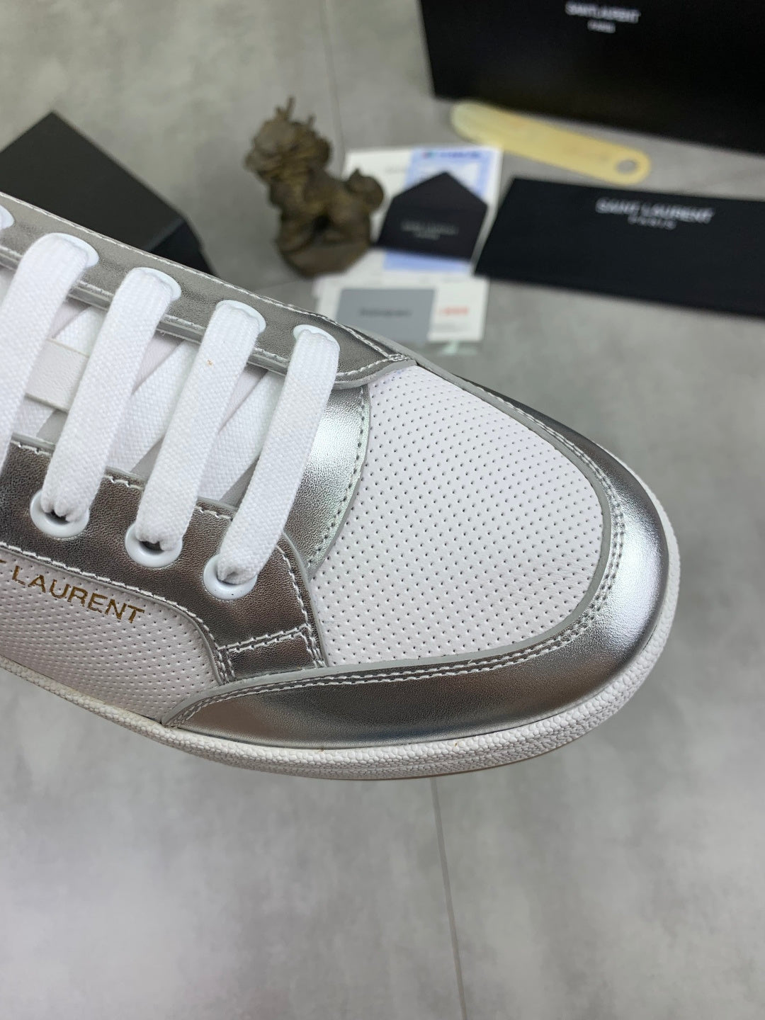 Close-up of white low-top sneaker toe with silver trim and white lace eyelets.