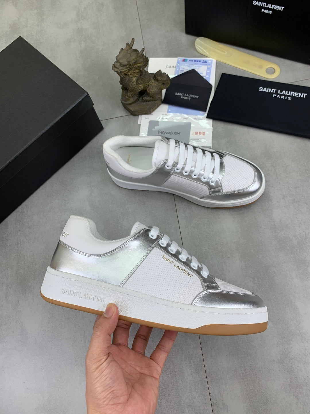 White low-top sneakers with silver side stripe, white laces, and rubber sole.