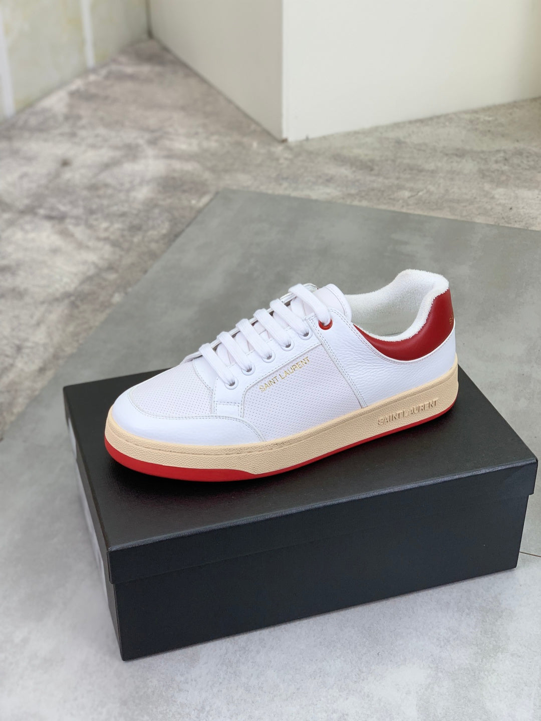White low-top sneaker with red heel collar and gum rubber sole.