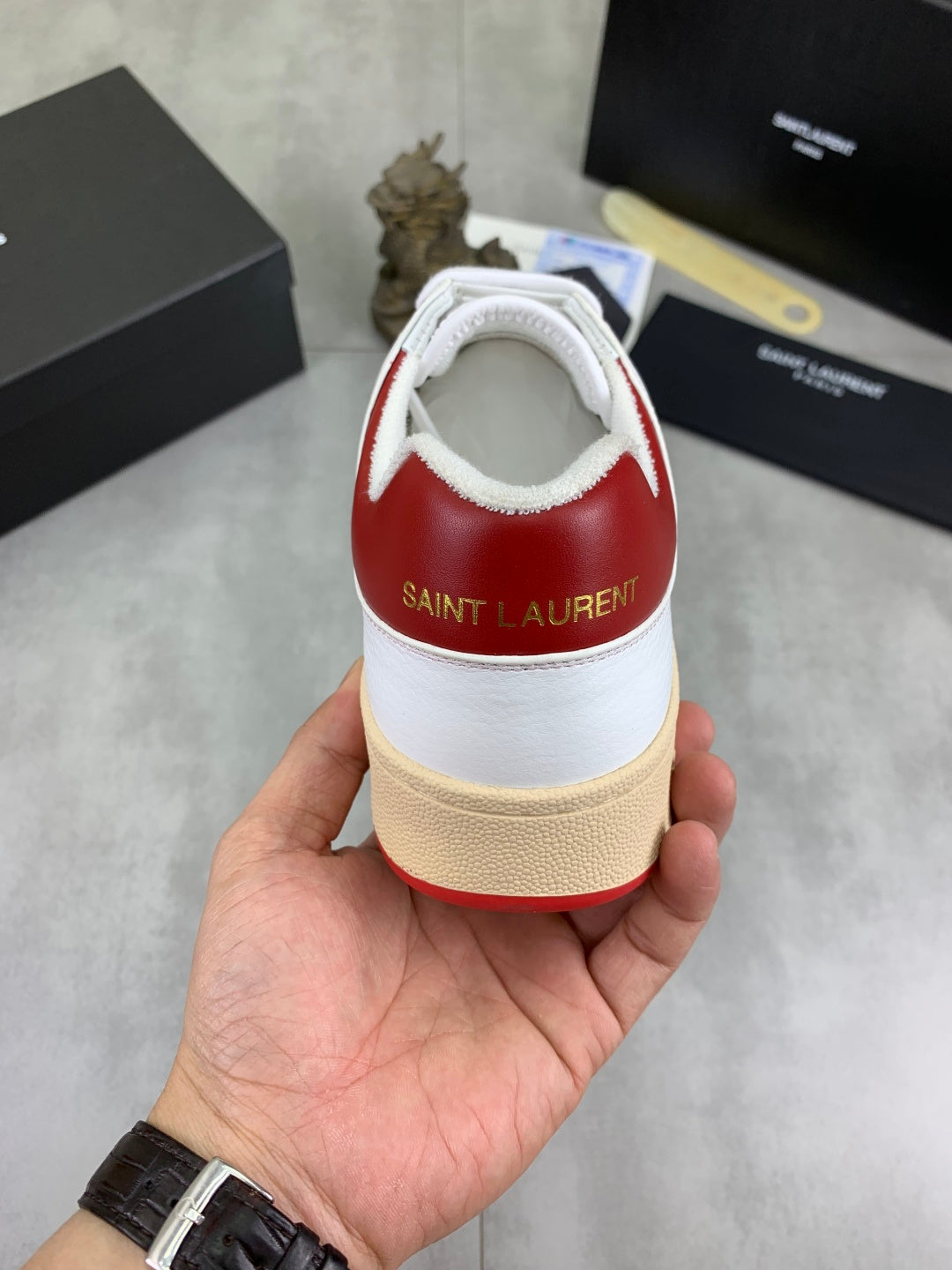 Back view of white sneaker with red heel collar and “Saint Laurent” logo.