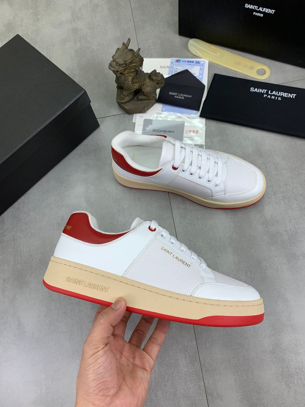 White sneakers with red heel accents, lace-up style, gum rubber soles.