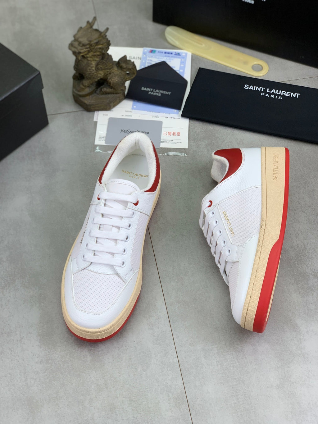 White sneaker with red side panel, lace-up front, and gum rubber sole.