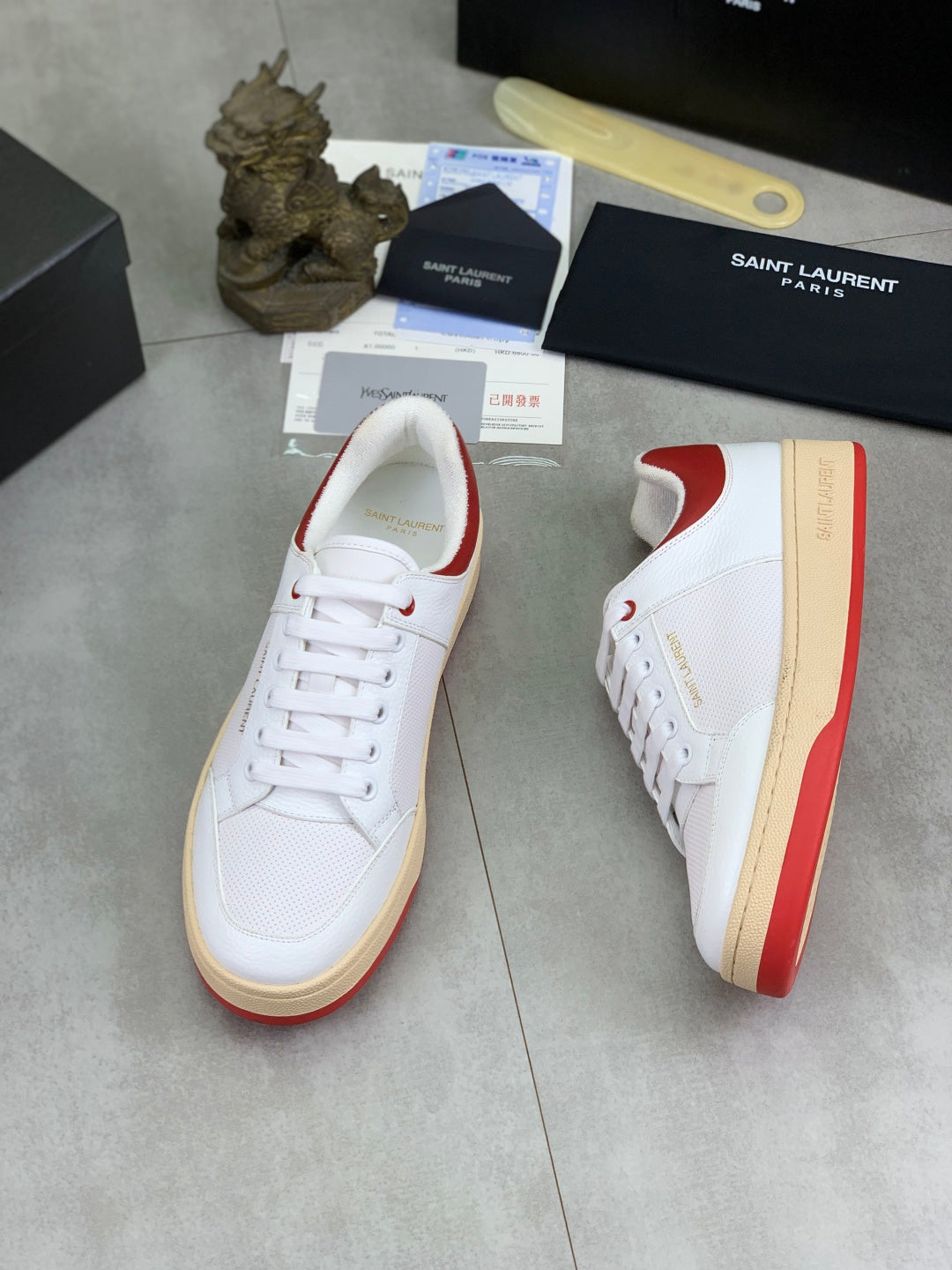 White sneaker with red side panel, lace-up front, and gum rubber sole.