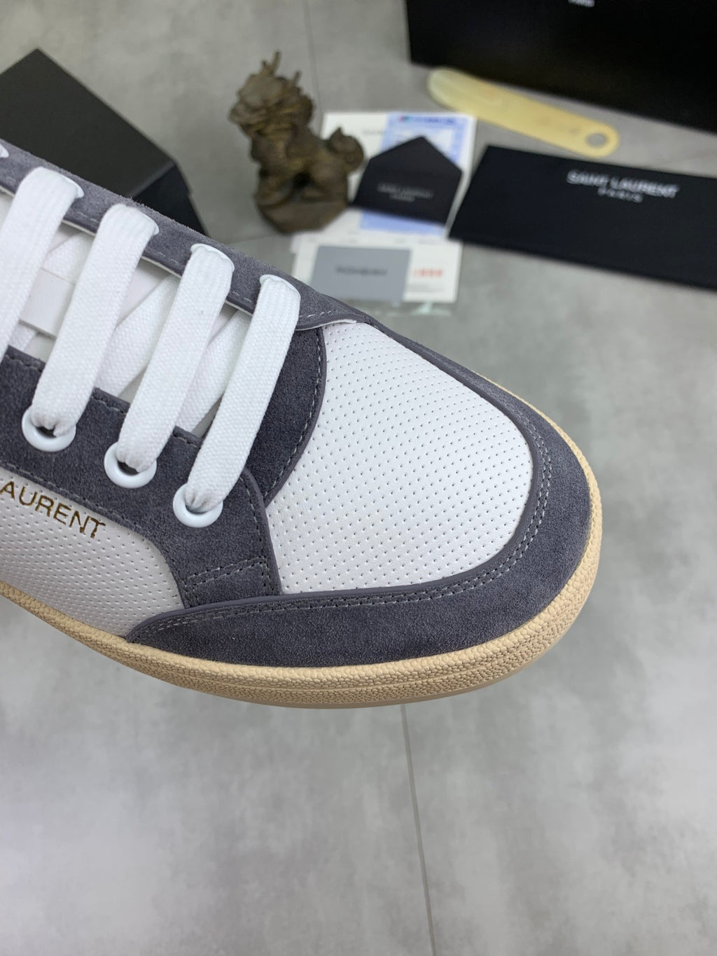 Low-top sneaker toe detail: white perforated fabric, navy suede, gum trim.