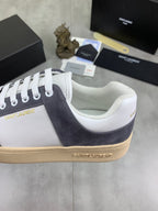 Low-top sneaker side close-up, white upper with navy suede quarter, gum sole.