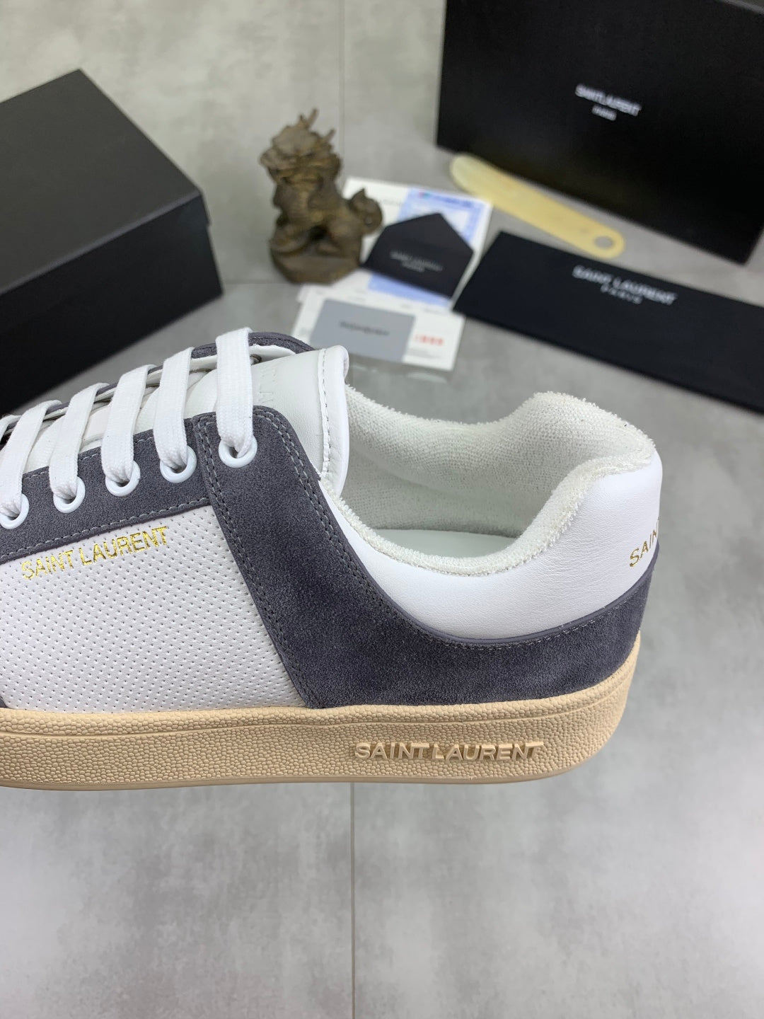 Low-top sneaker side close-up, white upper with navy suede quarter, gum sole.