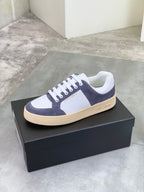 Low-top sneakers in navy and white with white laces and cream/tan sole edge.