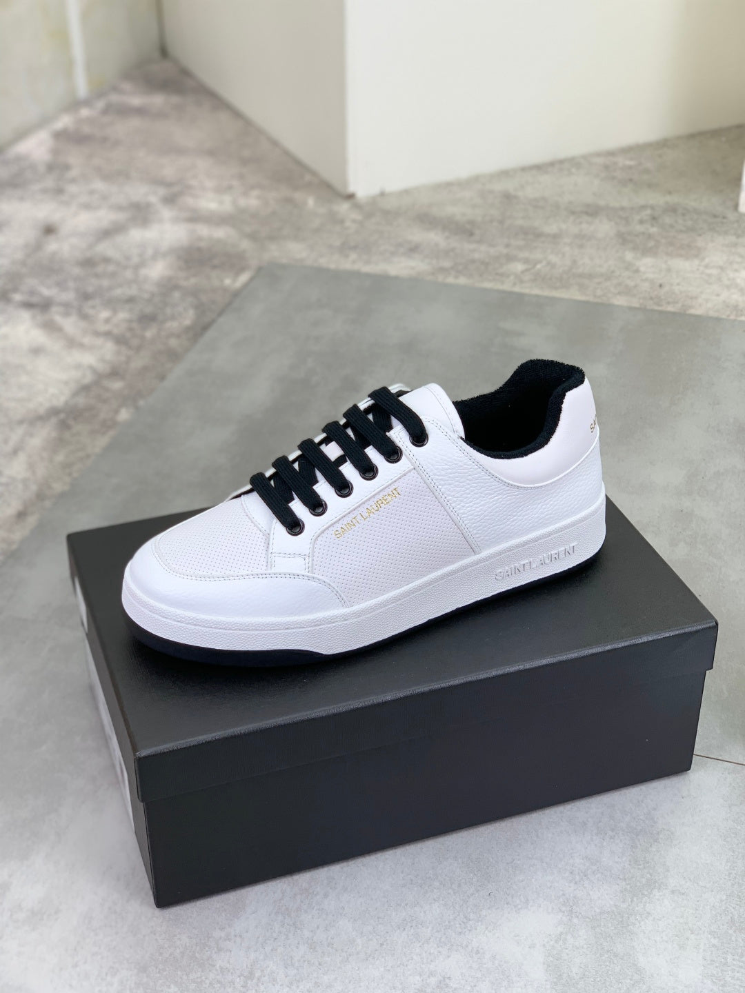 White low-top sneakers with black lace-up, side profile on a shoe box