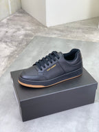 Black lace-up sneakers on a box, with textured upper and gum-brown outsole