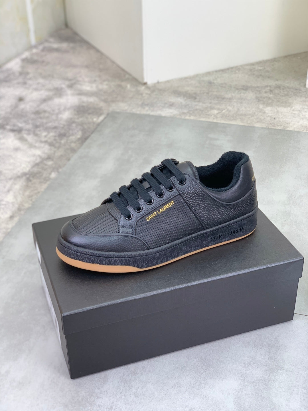 Black lace-up sneakers on a box, with textured upper and gum-brown outsole
