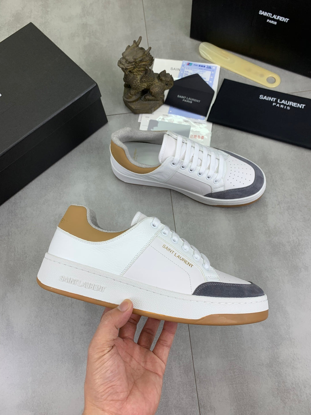 White lace-up sneakers with navy panels and gum sole, held for display