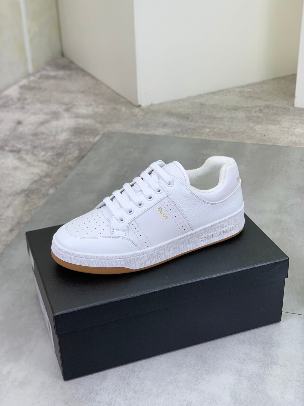 White lace-up sneakers on a dark shoe box with tan/gum sole edge