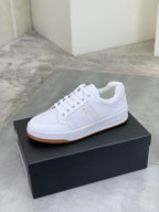 White lace-up sneakers on a dark shoe box with tan/gum sole edge