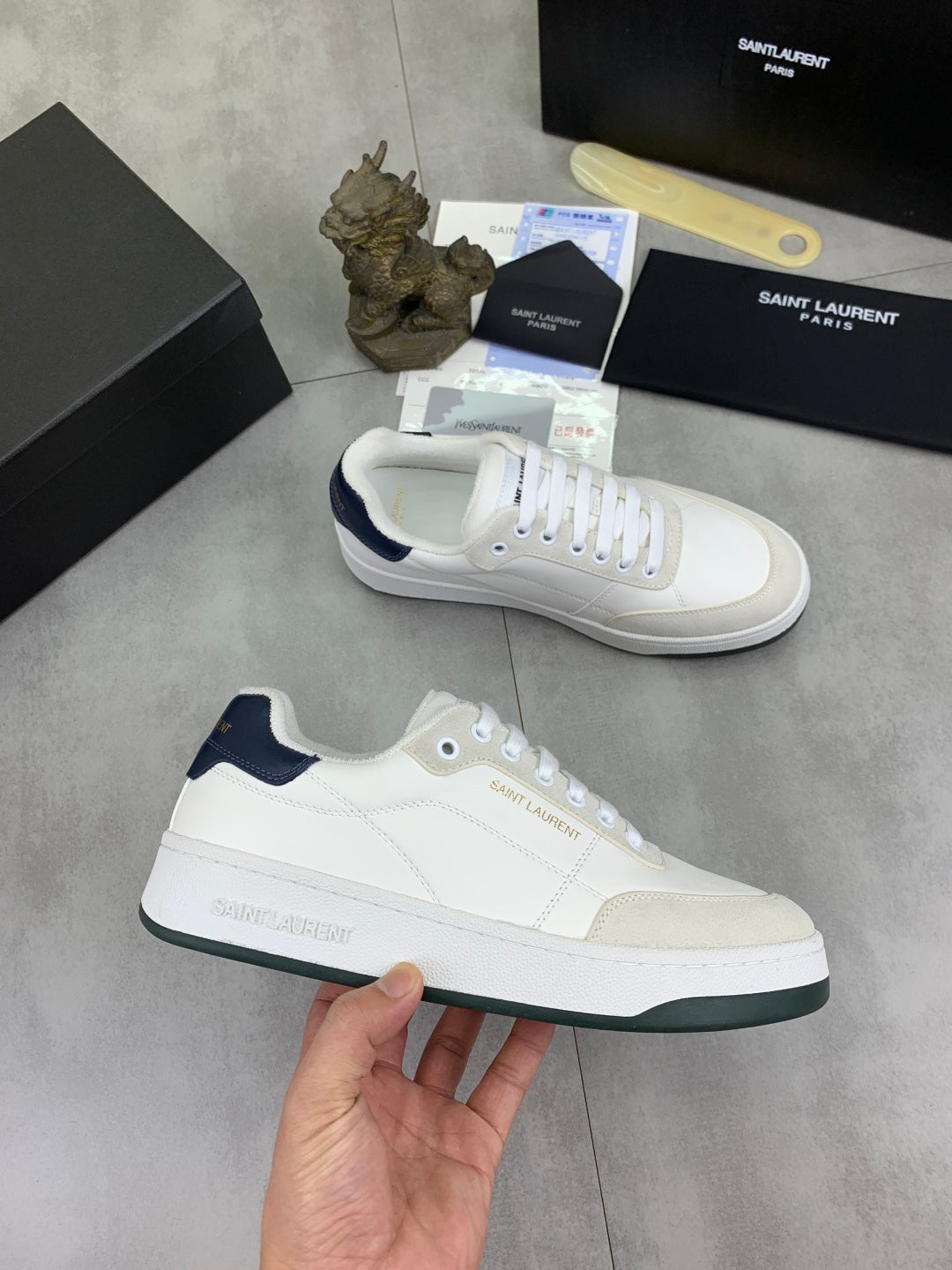 White low-top sneakers with navy trim, white laces, and Saint Laurent logo
