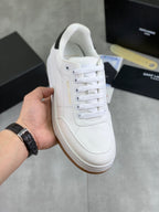 White low-top sneakers, white laces and gum sole, held in hand.
