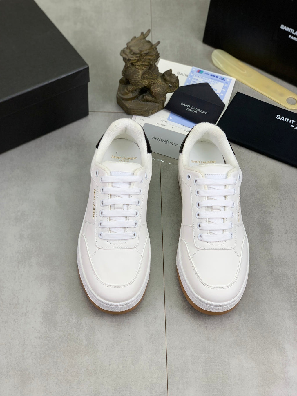 Pair of white low-top sneakers with white laces and gum soles on display.