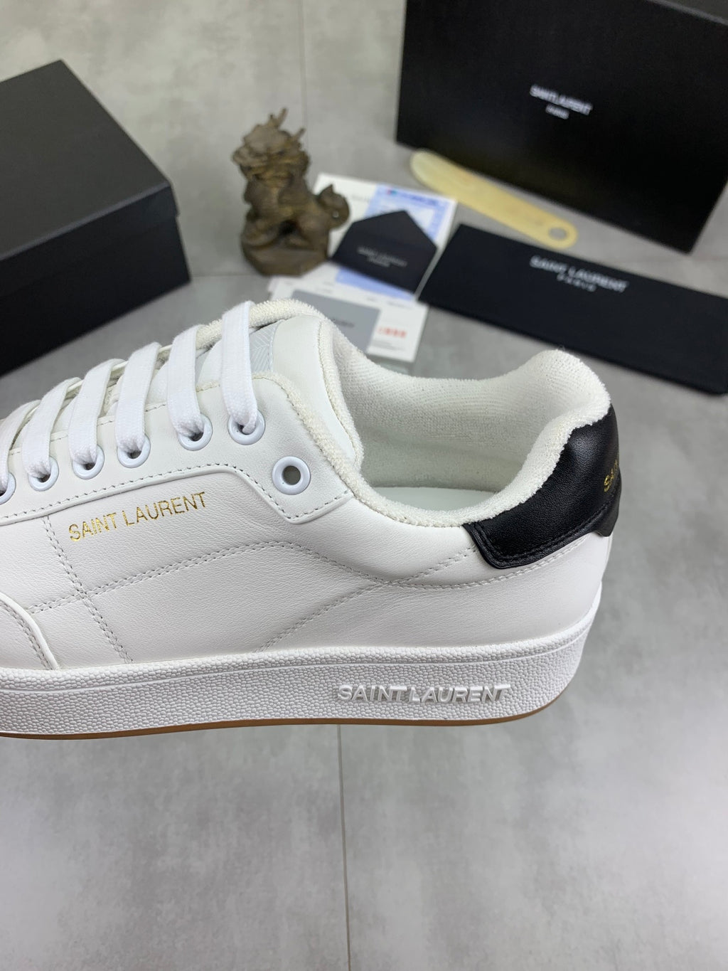 White sneaker side view with black heel panel and Saint Laurent logo.