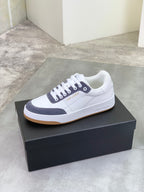 Unisex low-top sneakers on box, white leather with navy stripe and gum sole.