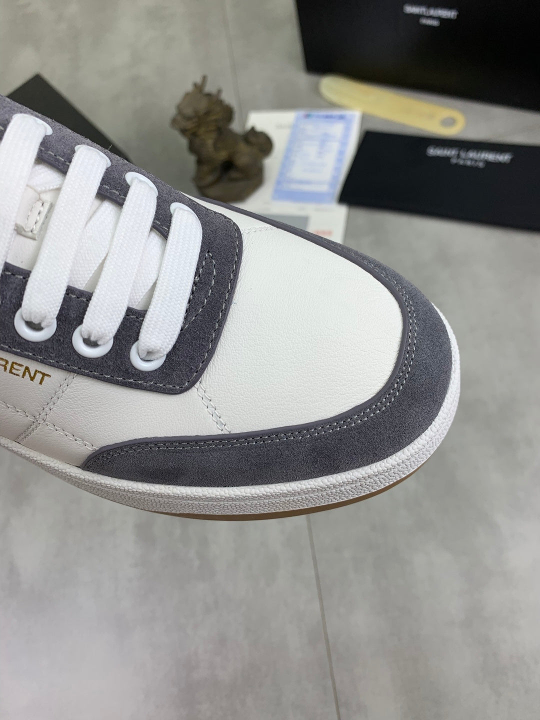 Unisex sneaker side close-up, white leather with navy suede panel and lace eyelets.