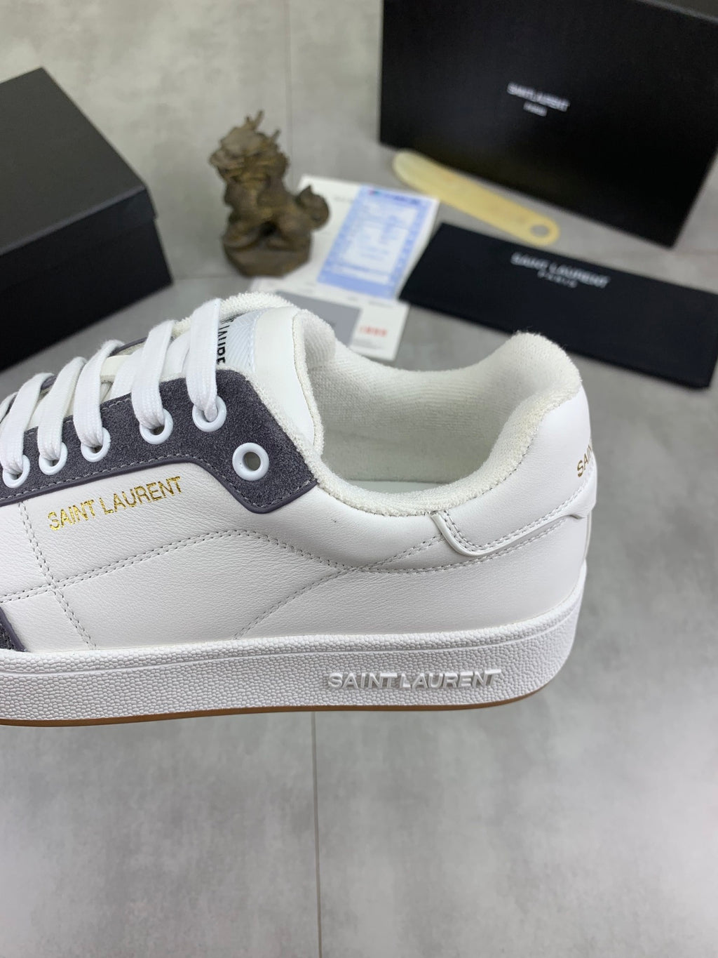 Unisex sneaker heel close-up, white leather with navy collar and logo detail.