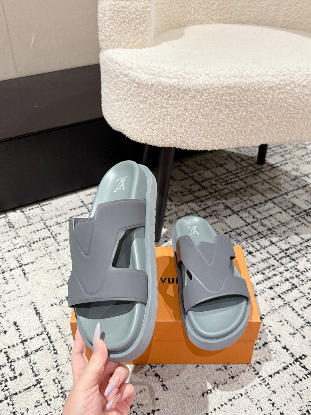 Light blue Louis Vuitton slide sandals with LV logo, held above orange box