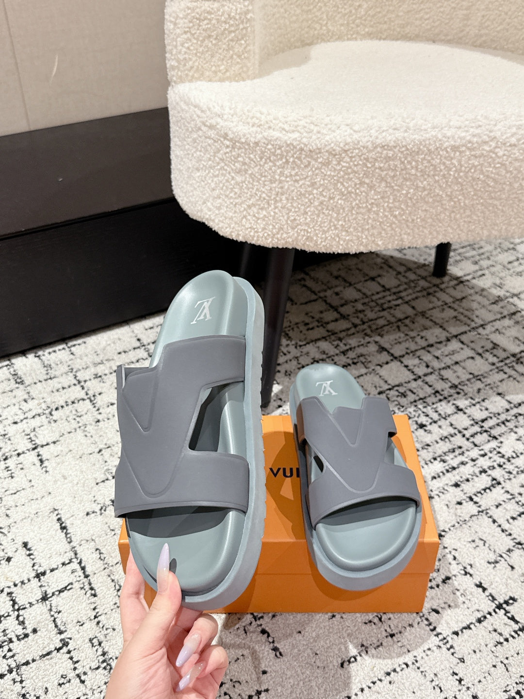 Light blue Louis Vuitton slide sandals with LV logo, held above orange box