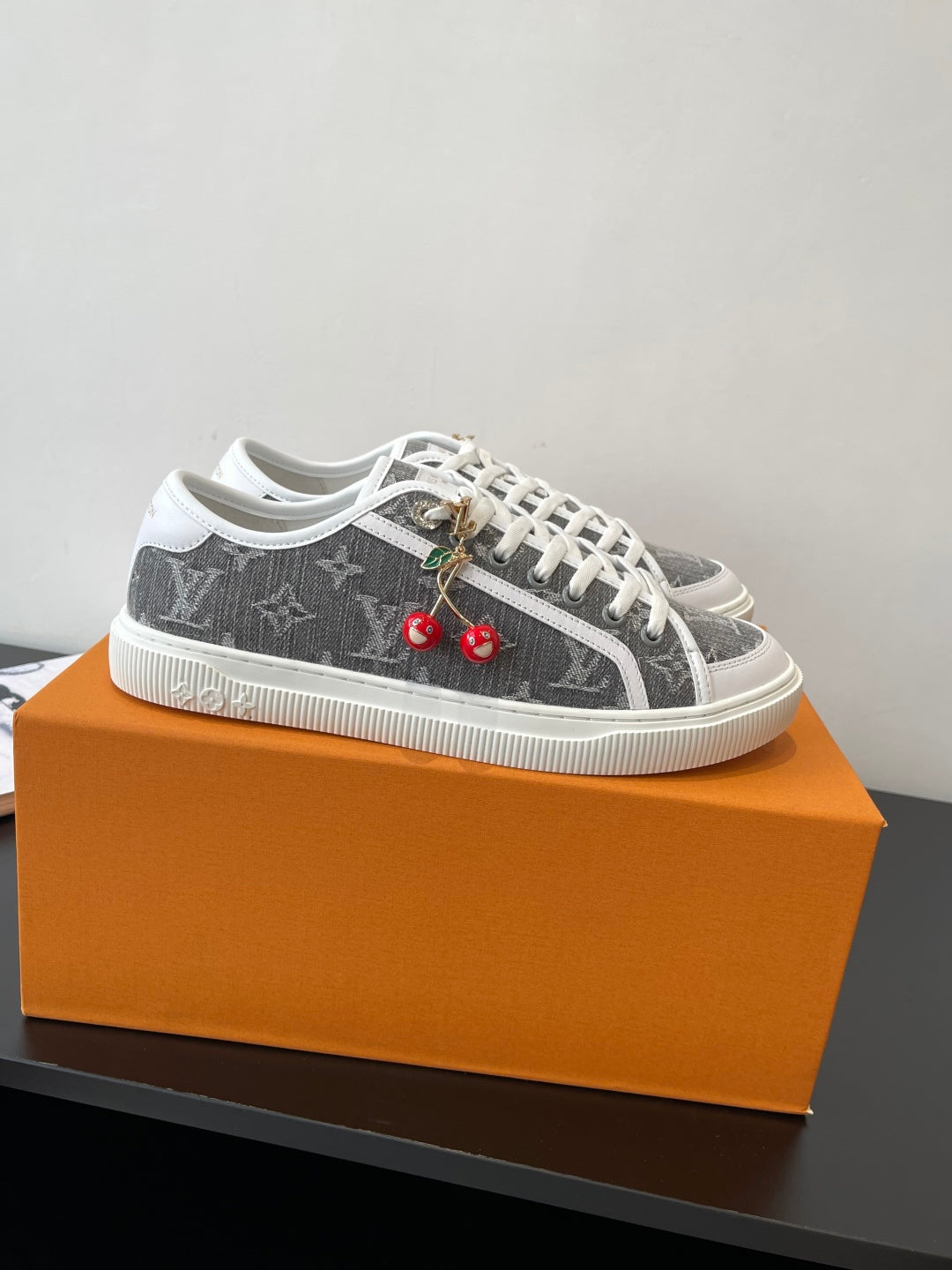 Women’s low-top sneakers with dark monogram print, white laces, cherry charm detail.