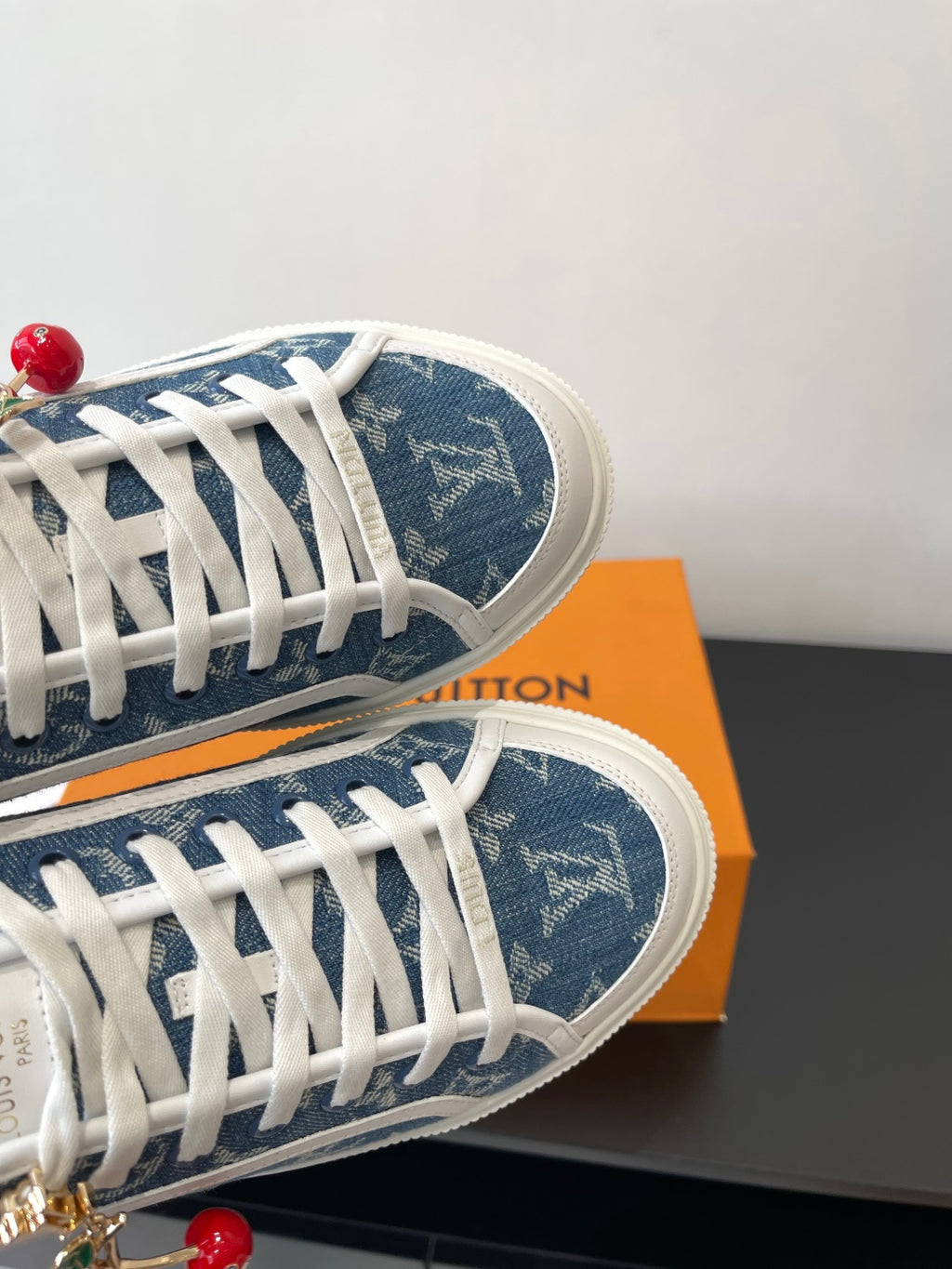 Louis Vuitton low-top sneakers close-up of blue monogram upper, white laces, and red charm