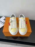 Louis Vuitton low-top sneakers with white laces, pale yellow panels, red charms