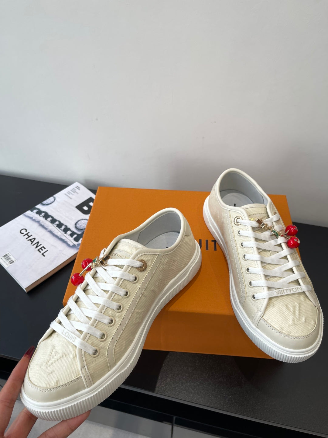 Women's Louis Vuitton sneakers, angled view, beige uppers with white laces and red charms.