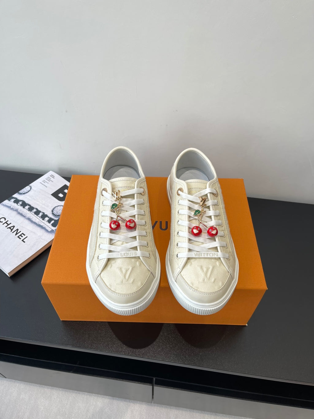 Women's Louis Vuitton sneakers, beige with white laces and red charm accents.