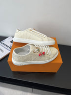 Women's Louis Vuitton sneakers, top view pair with beige uppers and red charm accents.