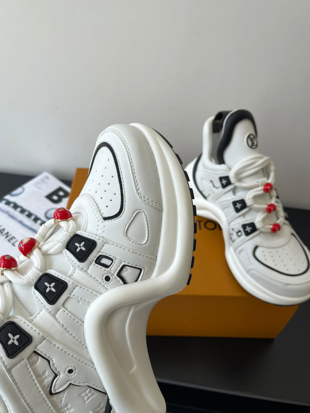White sneaker side and heel with embossed logo, black tab, red lace beads