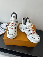 White low-top sneakers with black trim, LV tongue logos, red beaded lace accents
