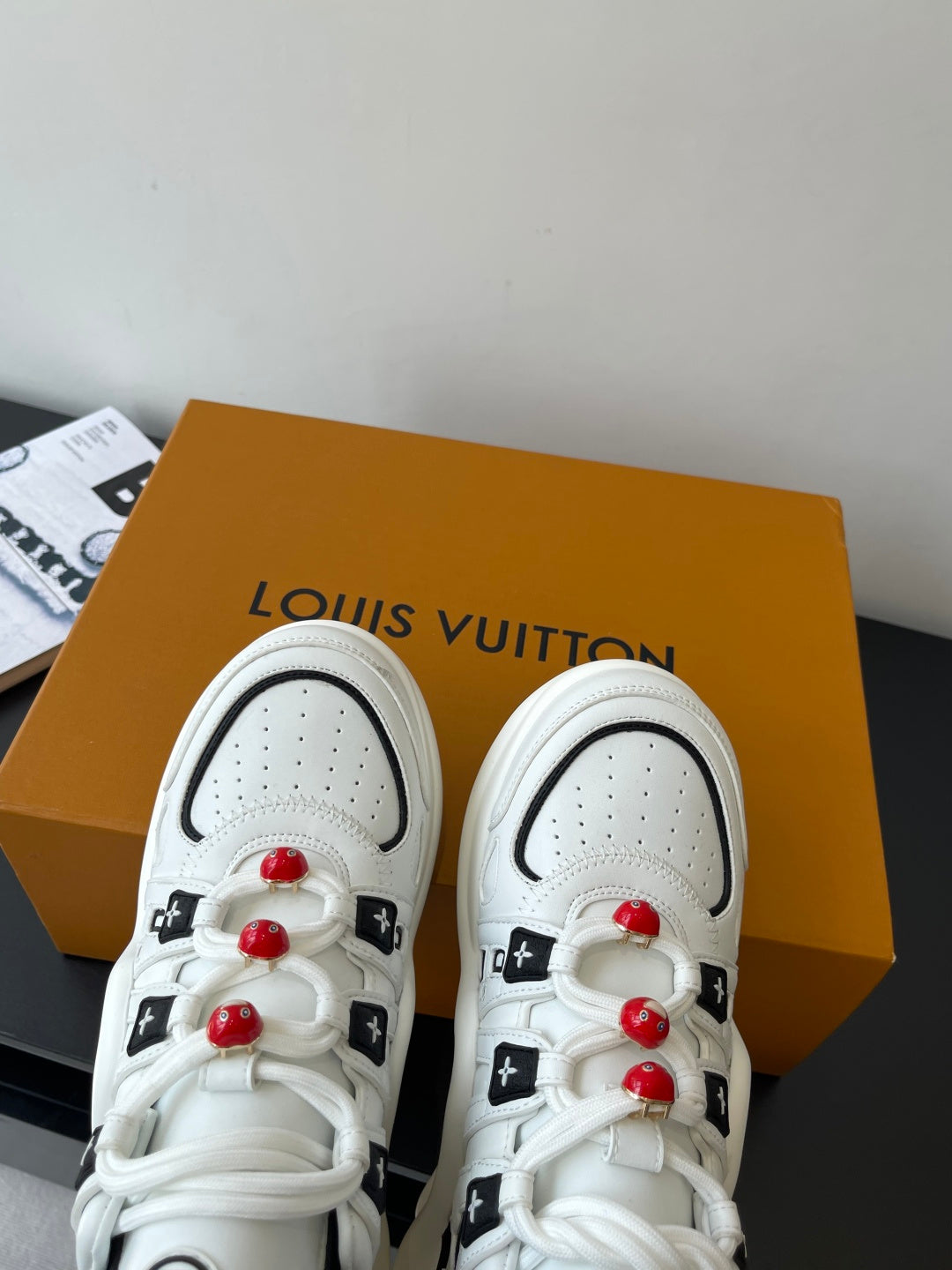 White low-top sneakers with perforated toe and red beaded lace accents