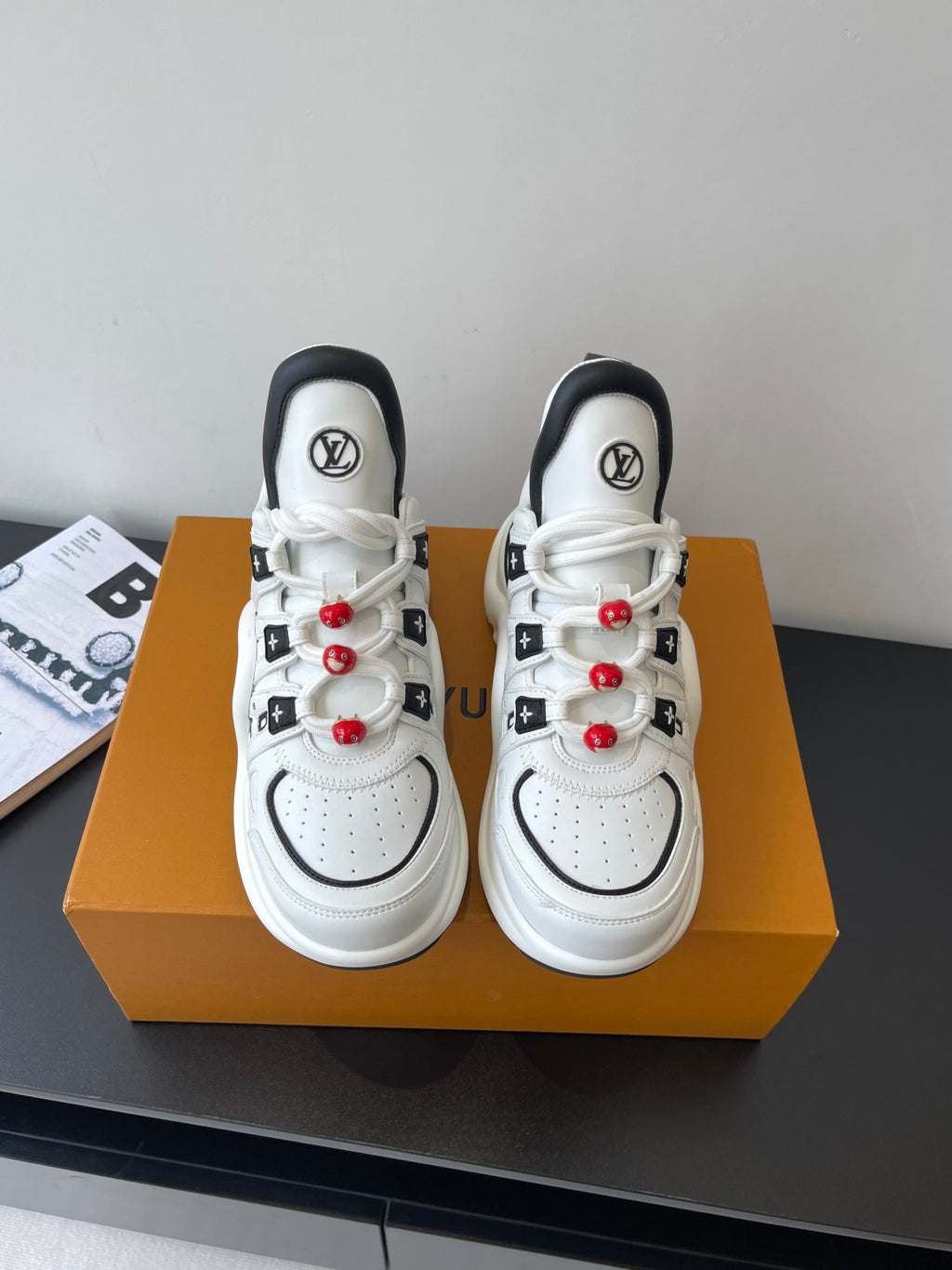 White low-top sneakers with black trim, LV logos, red beaded lace accents