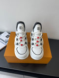 White low-top sneakers with black trim, LV logos, red beaded lace accents