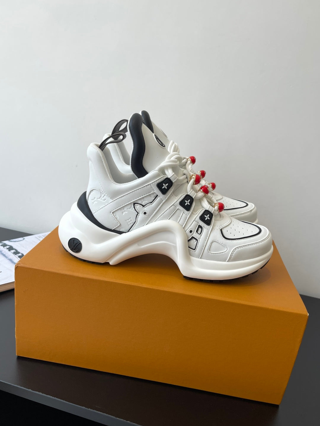 White low-top sneakers with black collar, padded sole, red beaded lace charms