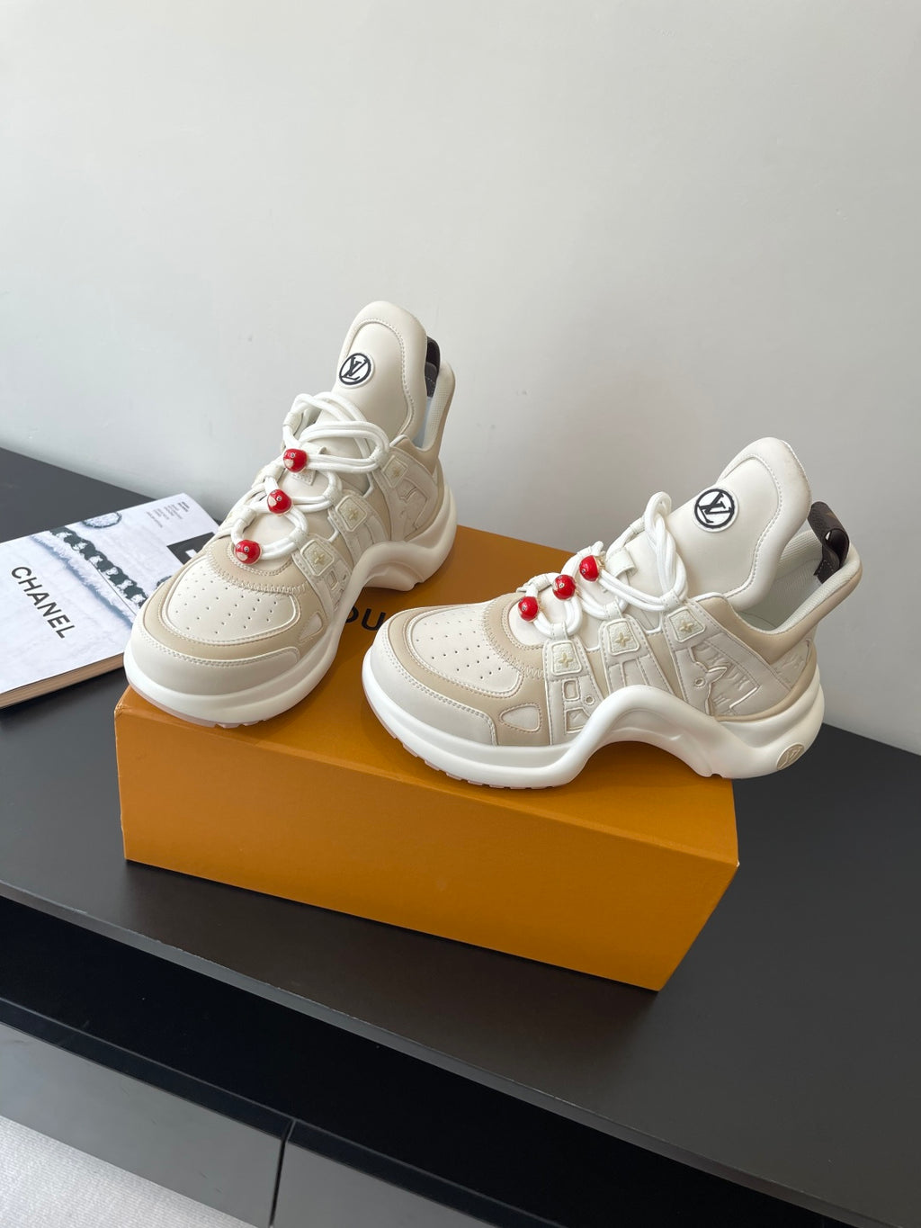 Two white chunky sneakers with lace-up design and red bead lace charms