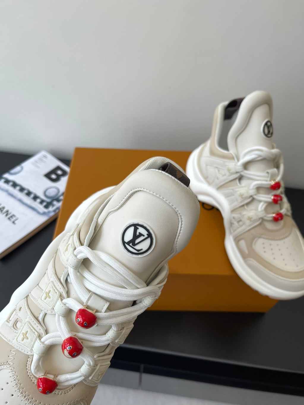 White sneaker toe and lace area with LV logo patch and red bead lace charms