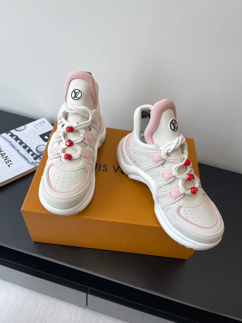 White and pink lace-up sneakers with red pom-poms and LV logos on tongues