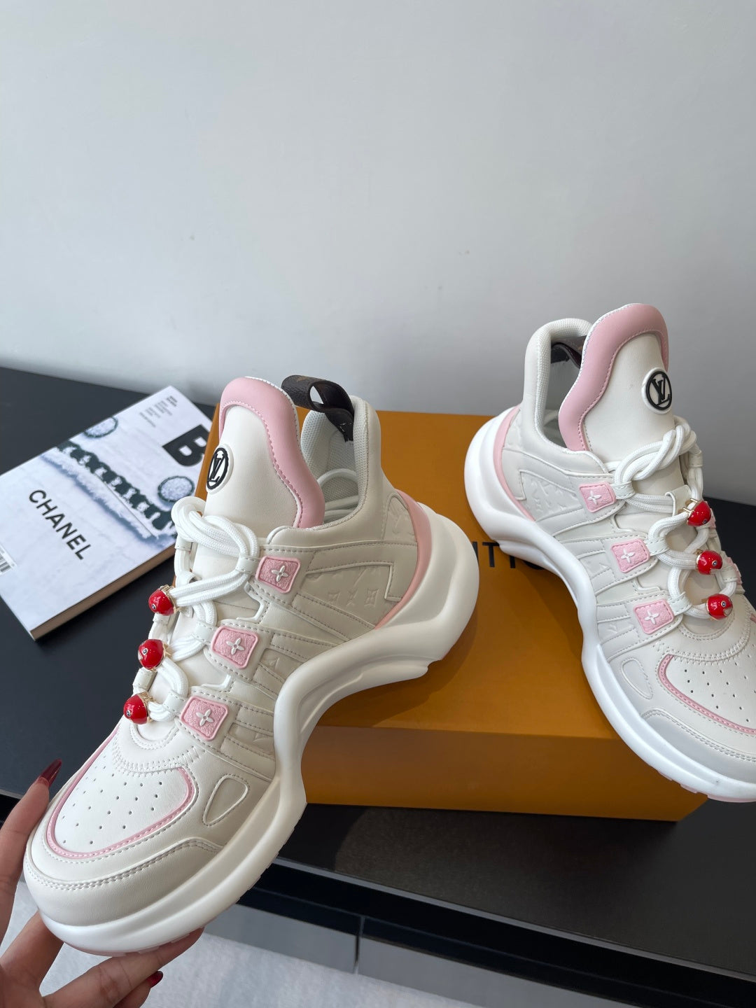 White and pink sneakers with perforated toe, red pom-poms, and LV logos on side
