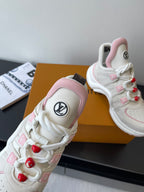 White lace-up sneaker with pink collar lining, red pom-poms, and LV emblem on tongue