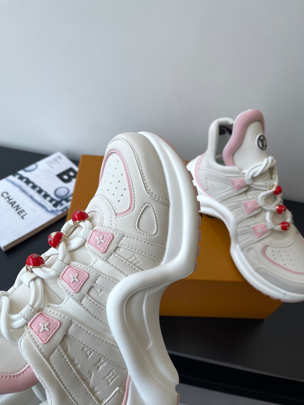 White and pink sneakers with thick sole, red pom-poms, and LV side logo