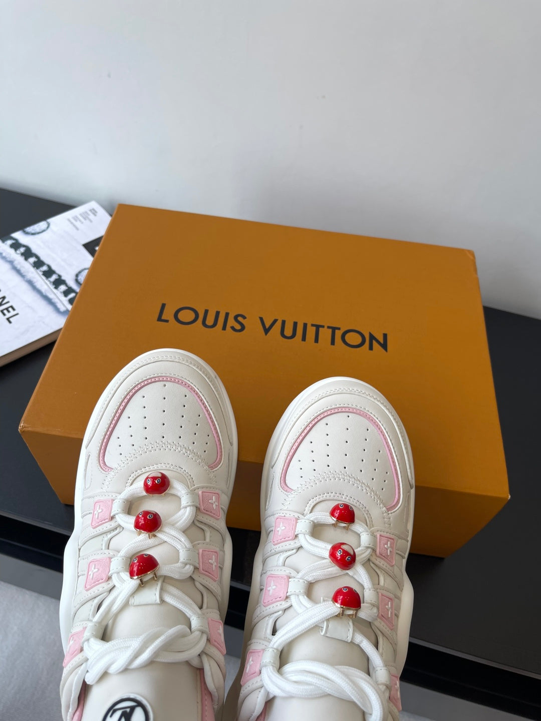 White sneakers with pink accents, lace-up eyelets, and red pom-poms