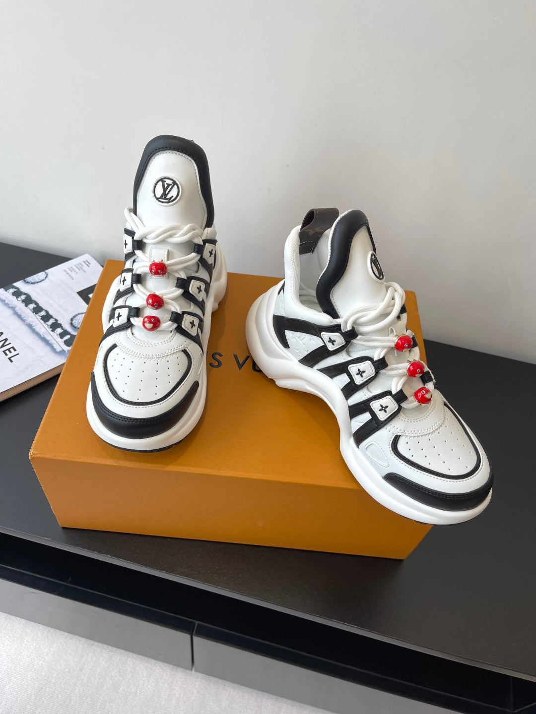 White and black sneakers pair with black strap details and red beaded lace accents