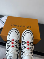 White and black sneakers on box with black strap details and red lace charms