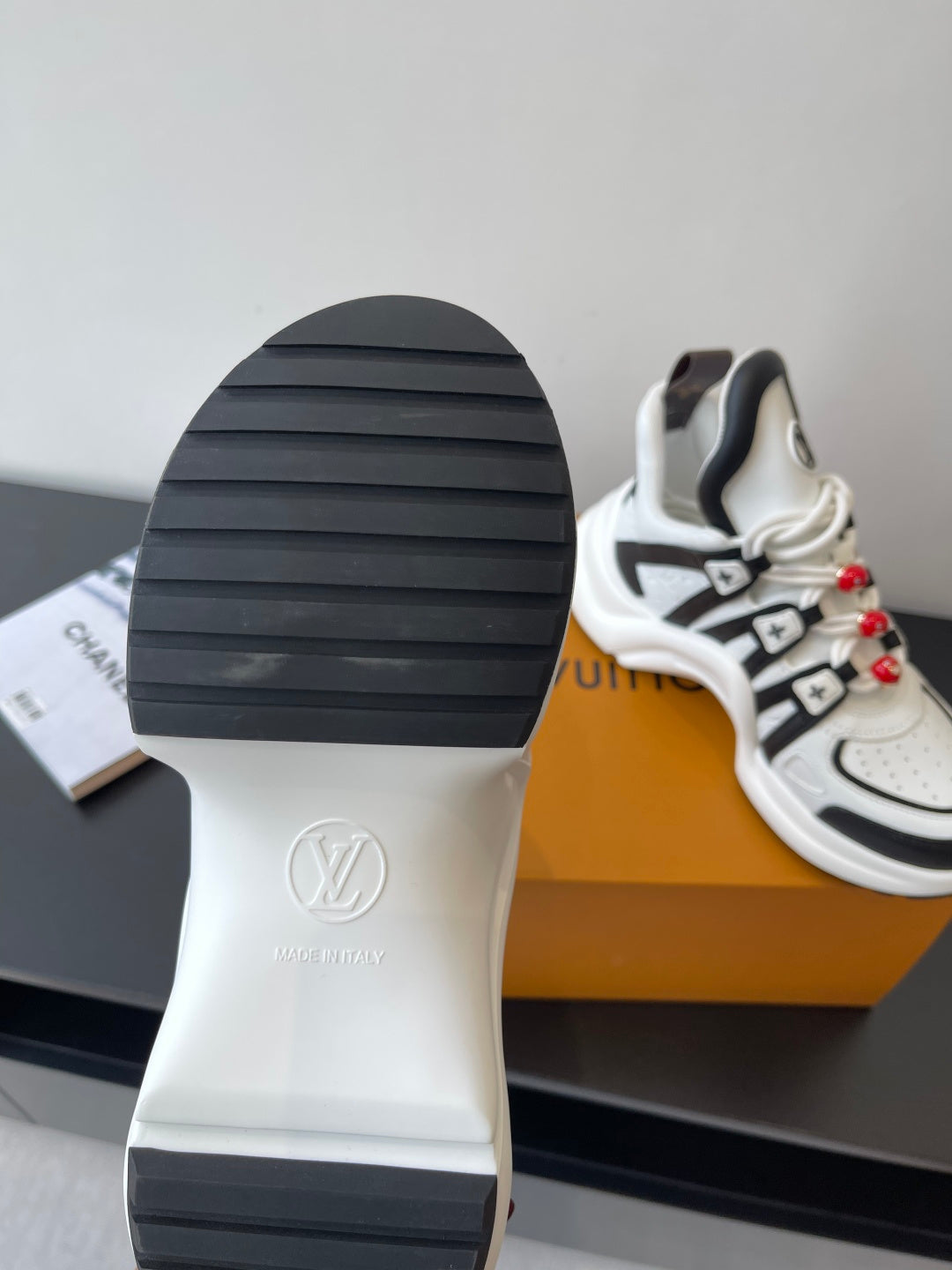 White sneaker outsoles with black tread, featuring an LV logo on the heel